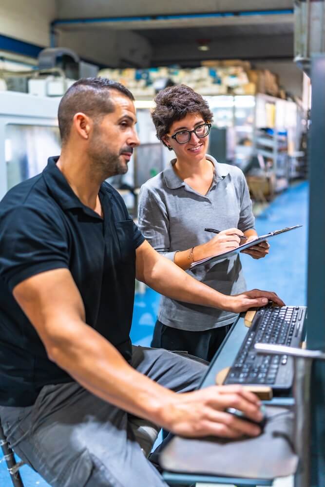 Engineer showing computer screen data to female manager at factory